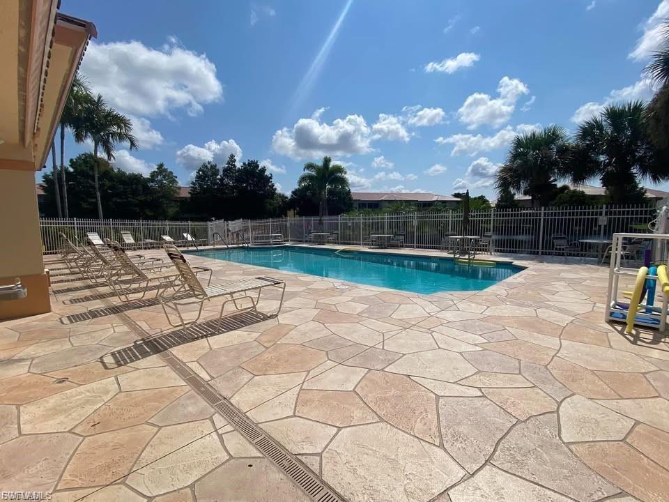 Outdoor swimming pool featuring a patterned paver deck, perimeter fencing, and surrounding palm trees