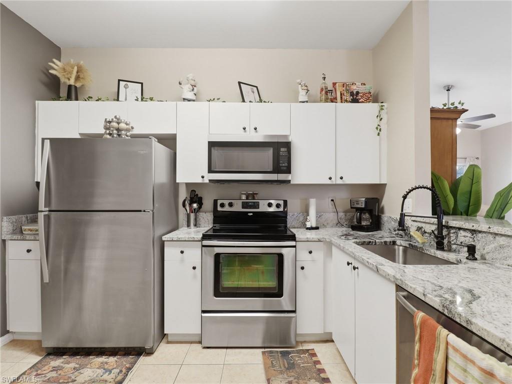 Kitchen featuring white cabinetry, light-toned granite countertops, and stainless steel appliances including a refrigerator, range, and microwave