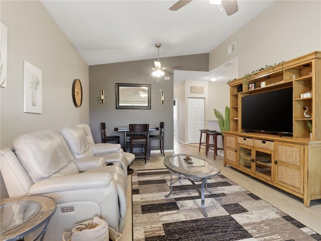 Living area featuring light wood-finish flooring, a vaulted ceiling with two ceiling fans, and a media console with integrated storage
