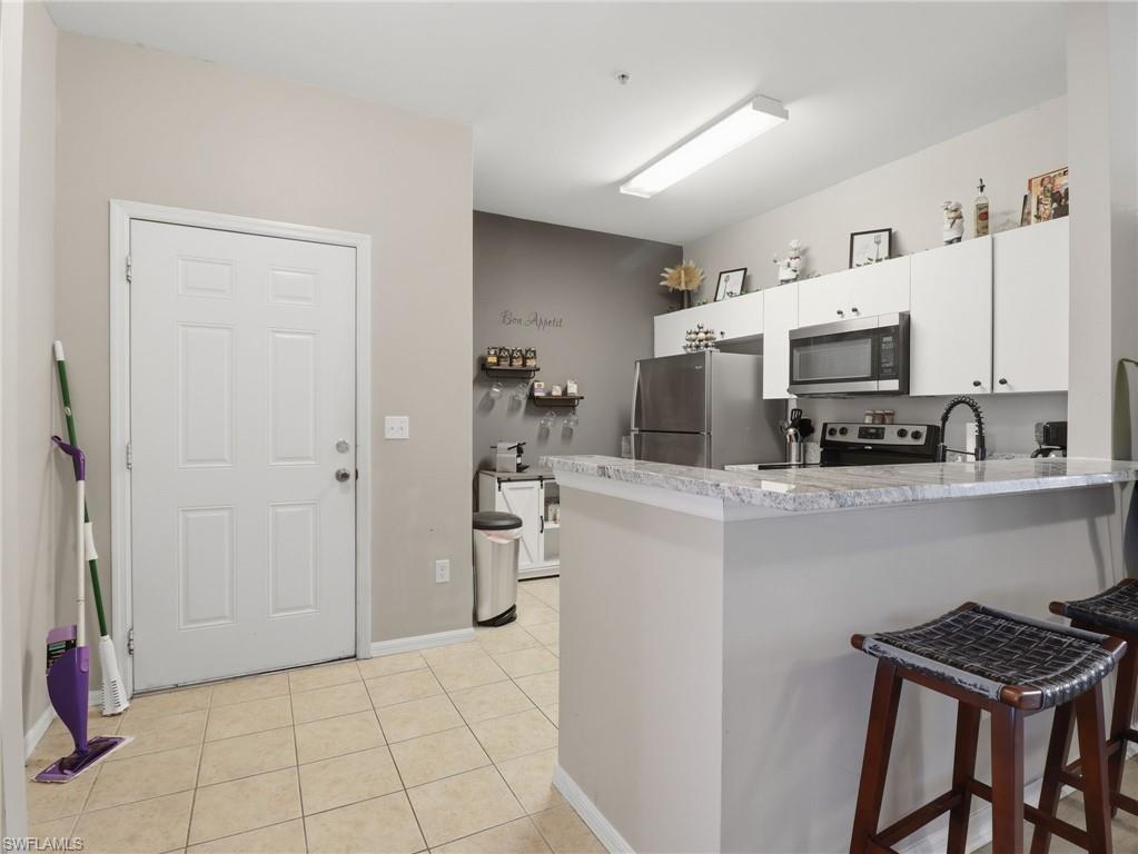 Kitchen featuring stainless steel appliances, white cabinetry, a bar-height countertop, and tile flooring