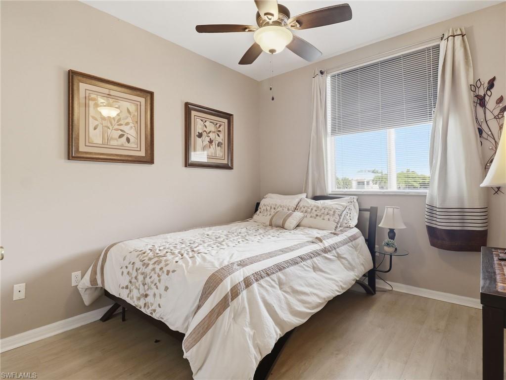Room featuring wood-finish flooring, a ceiling fan with integrated lighting, and a large window with blinds