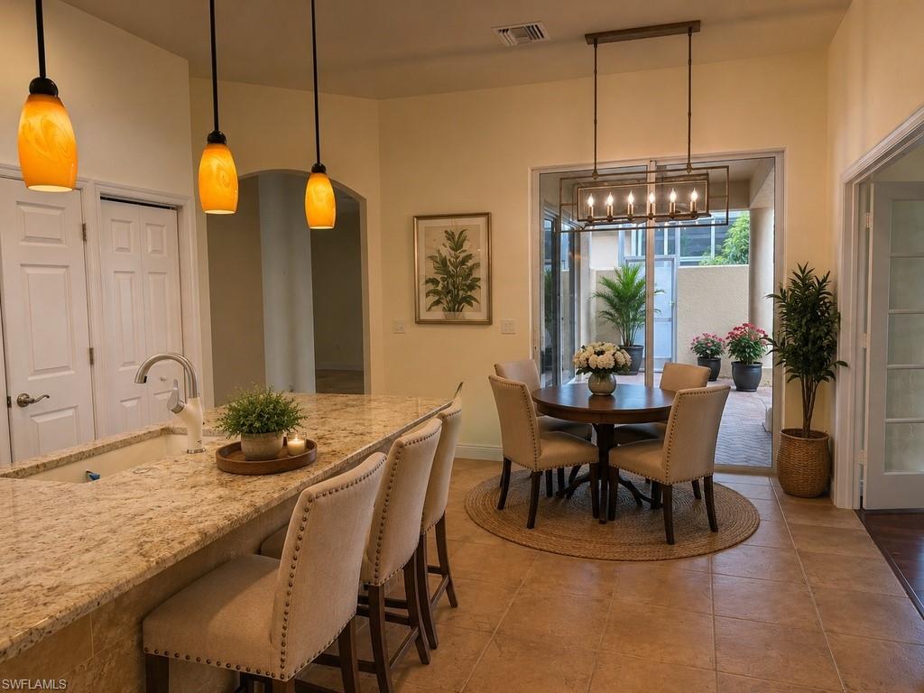 Kitchen and dining area featuring a granite-top island with integrated sink, three pendant lights, and tile flooring