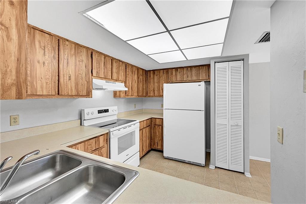 Kitchen featuring white appliances, light countertops, brown cabinets, under cabinet range hood, and light tile patterned flooring