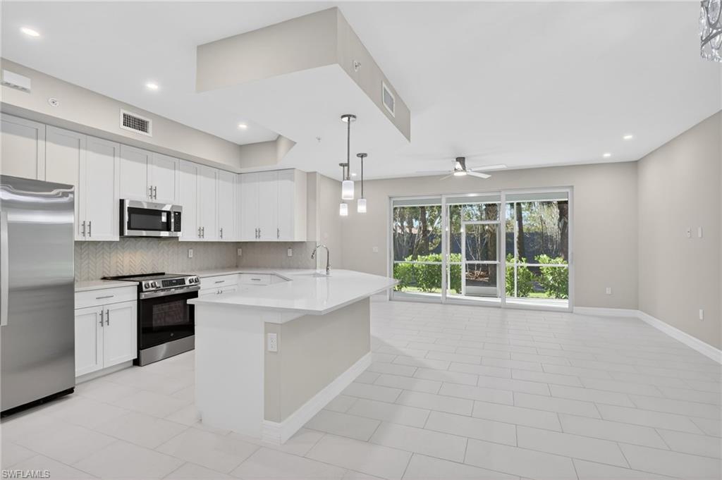 Open-concept kitchen and living area featuring a central island with pendant lighting, stainless steel appliances, white cabinetry, and wood-finish tile flooring