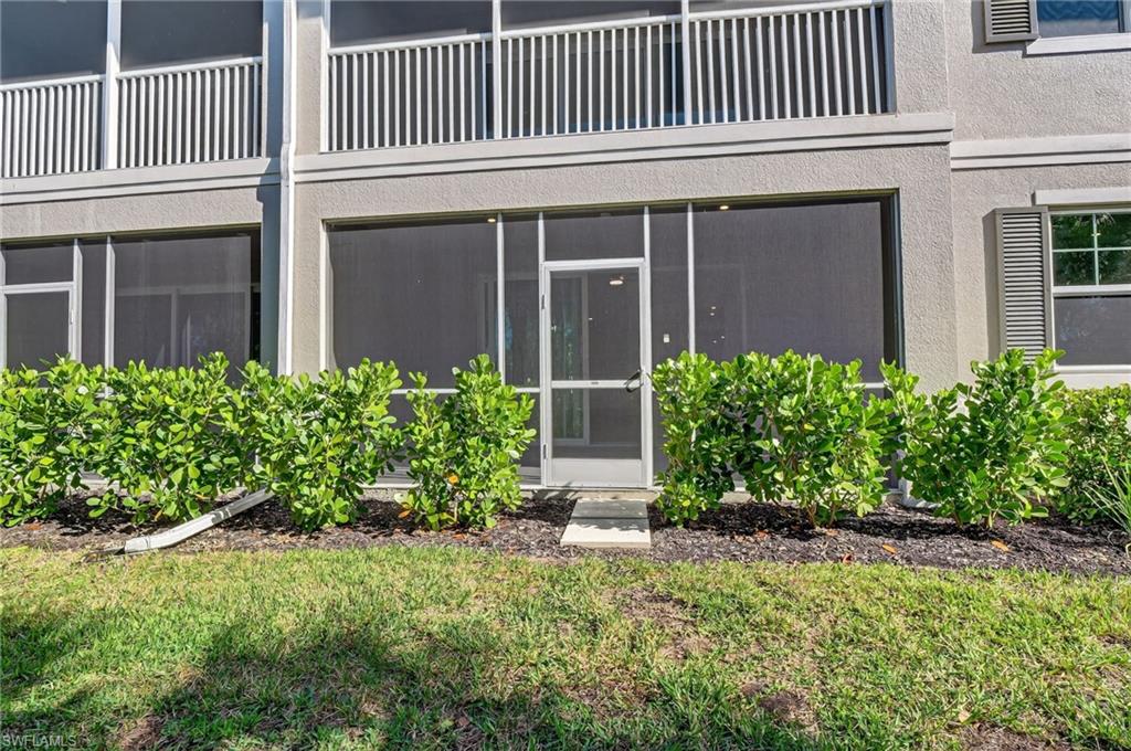 Ground-level screened patio with exterior access, surrounded by manicured shrubs
