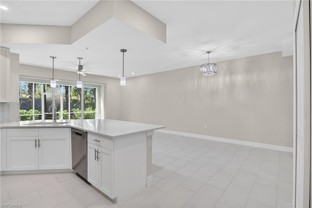 Open-concept kitchen and living area featuring white shaker cabinetry, an island with a quartz countertop, stainless steel appliances, and tile flooring