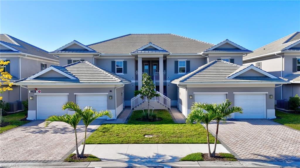 Contemporary multi-level residence featuring a tile roof, stucco exterior, two-car garage, paver driveway, and a manicured lawn with tropical landscaping