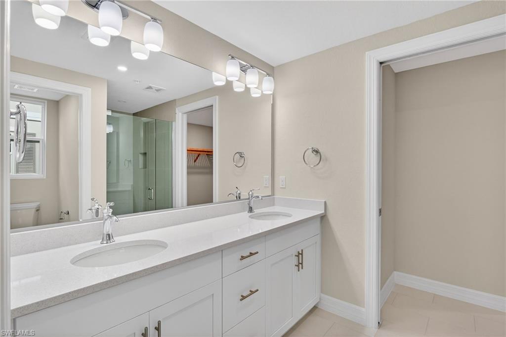 Dual vanity with undermount sinks, white cabinetry with gold-finish hardware, and a light-toned countertop