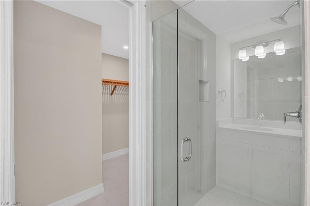 Contemporary bathroom featuring a glass-enclosed shower with tile surround, a built-in shower niche, and a vanity with an integrated sink