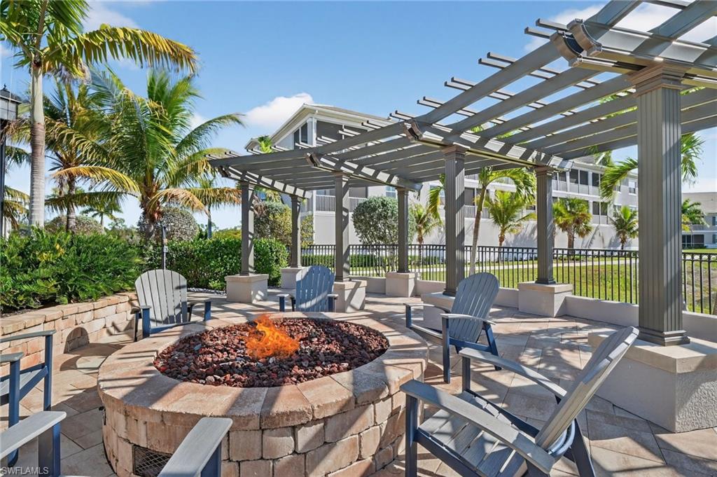 Outdoor fire pit area with stone pavers, a built-in stone fire pit, and a slatted pergola structure
