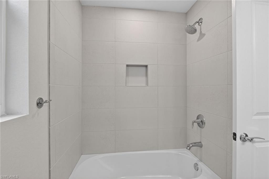 Bathroom featuring a white bathtub, light-toned tile surround, recessed shower niche, and polished chrome fixtures