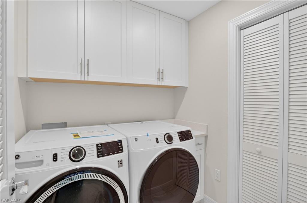 Laundry area featuring a pair of white front-load appliances, white upper cabinetry with brushed nickel hardware, a light-toned countertop, and a louvered bifold door