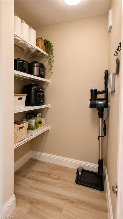 Walk-in pantry featuring light wood-finish flooring, white baseboards, and neutral wall paint
