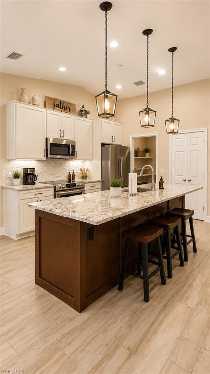 Open-concept kitchen featuring an oversized island with seating, pendant lighting, light-colored cabinetry, stainless steel appliances, and wood-finish flooring