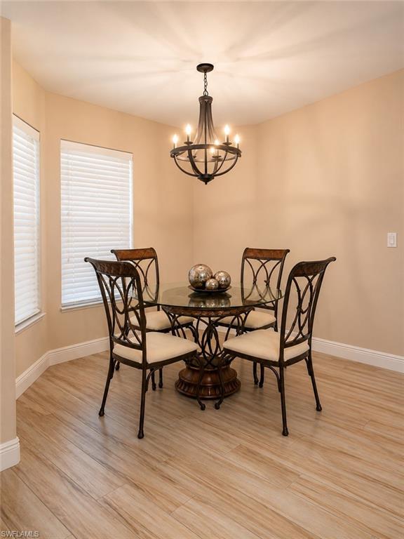 Bay window with blinds, wood-finish flooring, and a chandelier with ambient lighting