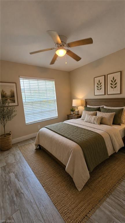 Bedroom featuring wood-finish flooring, a ceiling fan with light fixture, and a window with blinds