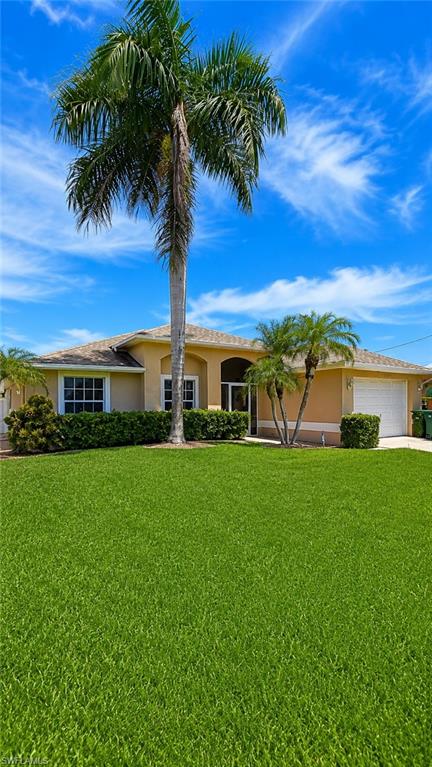 Tropical-inspired residence featuring a neutral-toned stucco exterior, a tile roof, a two-car garage, and a lush front lawn with mature palm trees