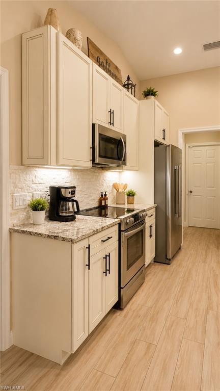 Kitchen featuring light-toned cabinetry with dark hardware, stone-finish countertops, stainless steel appliances, and wood-finish flooring