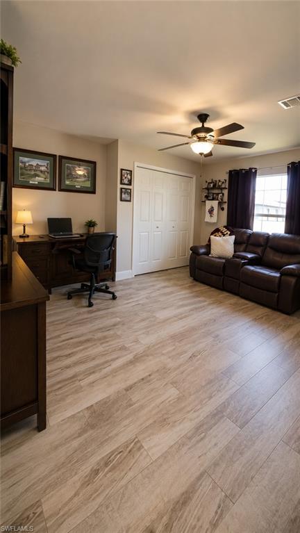 Spacious interior room featuring wood-finish plank flooring, a ceiling fan with integrated lighting, and a window with dark curtains