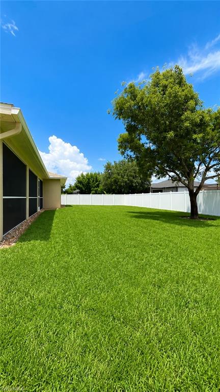 Spacious backyard featuring a manicured lawn, a white privacy fence, and mature landscaping