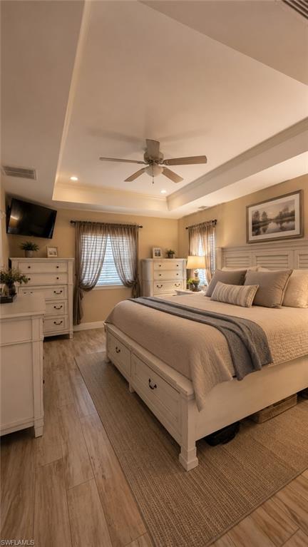 Tray ceiling with recessed lighting and a ceiling fan, wood-finish flooring, and window treatments
