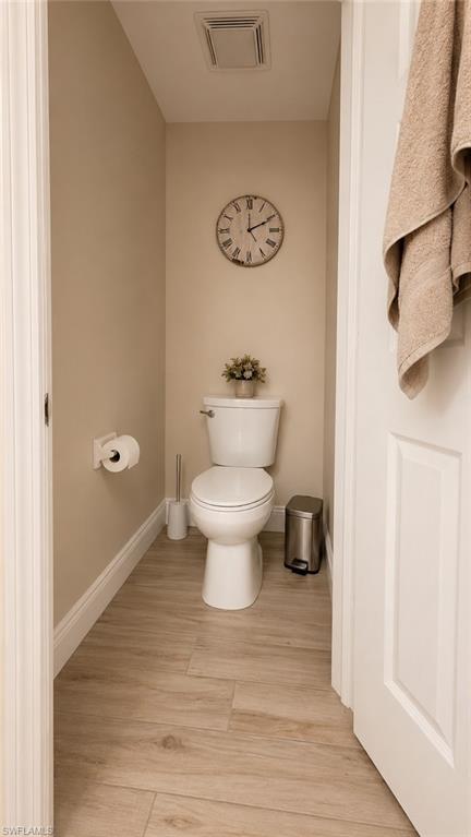 Powder room featuring wood-finish flooring, a white toilet, and neutral wall tones