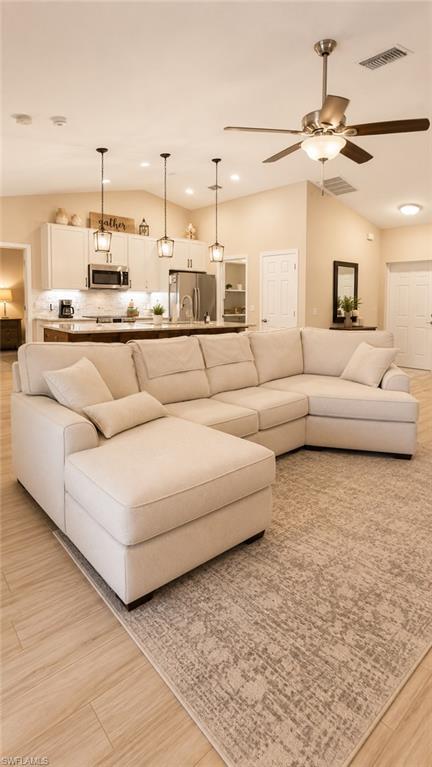 Open-concept living area featuring vaulted ceilings, wood-finish flooring, a ceiling fan, and recessed lighting