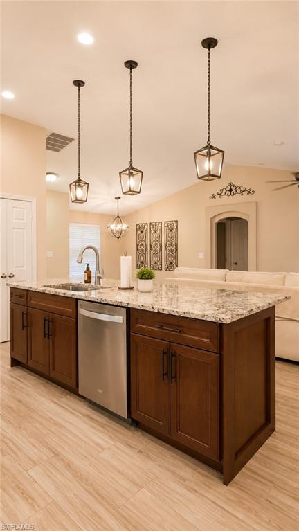 Kitchen island featuring granite-style countertops, an undermount sink with a gooseneck faucet, a stainless steel dishwasher, and dark wood cabinetry
