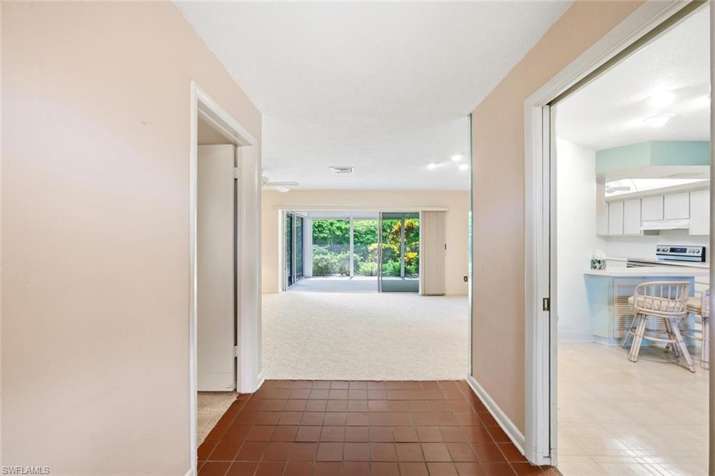Hallway featuring terra cotta tile flooring, leading to a living area with light-toned carpeting and sliding glass doors