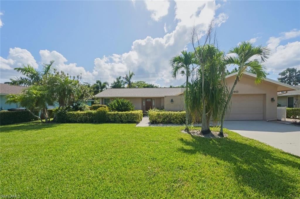 Single-story residence featuring a two-car garage, mature palm trees, sculpted hedges, and a verdant lawn