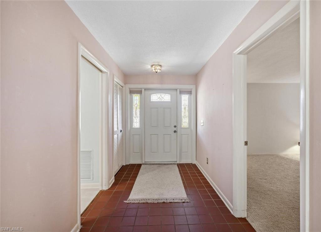 Entryway featuring terracotta-style tile flooring, a paneled front door with decorative glass inserts, and sidelight windows