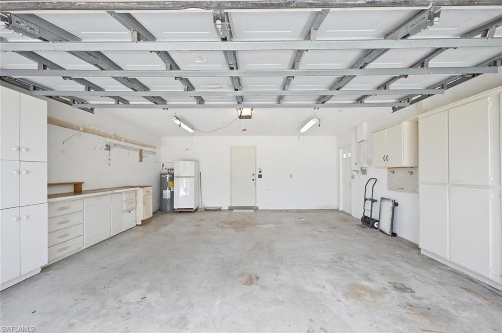 Expansive garage space featuring a concrete floor, extensive built-in white cabinetry, a built-in workbench, and overhead lighting