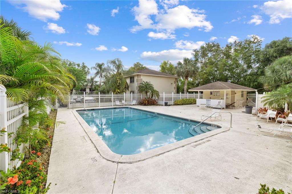 Fenced swimming pool with concrete decking, surrounding tropical landscaping, and an adjacent cabana structure