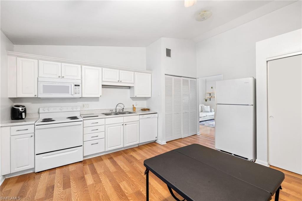Kitchen featuring wood-finish flooring, white cabinetry, a built-in microwave, and a refrigerator