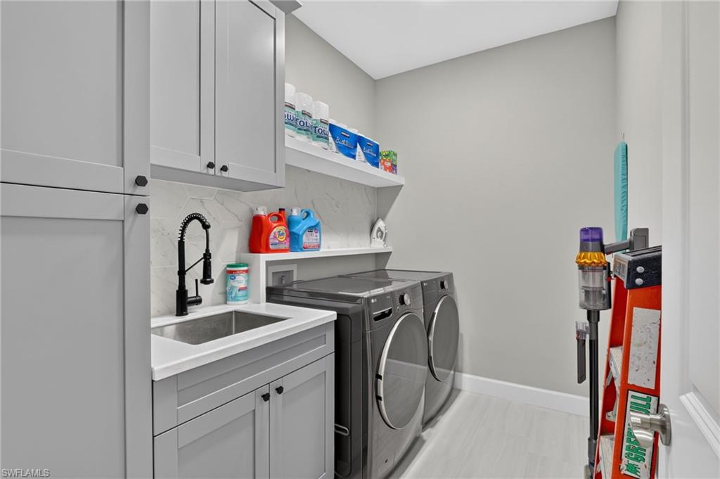 Laundry room featuring light gray cabinetry, a built-in sink with a matte black faucet, white countertops, and a white floating shelf