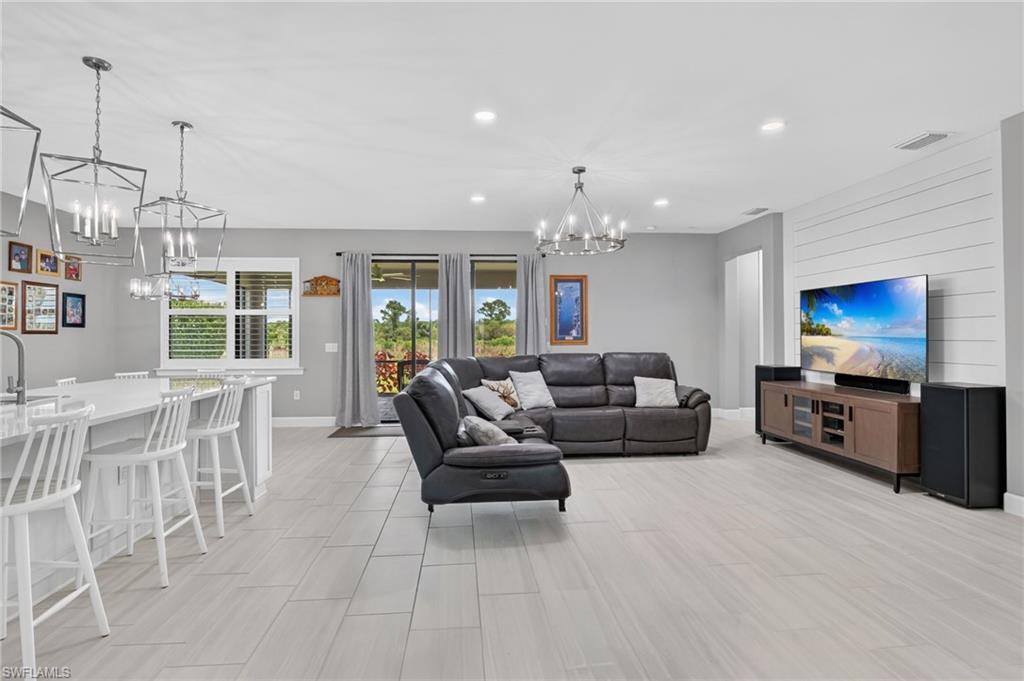 Open-concept interior featuring light plank-style flooring, a kitchen island with seating, pendant lighting, recessed ceiling lights, and a shiplap-accented wall