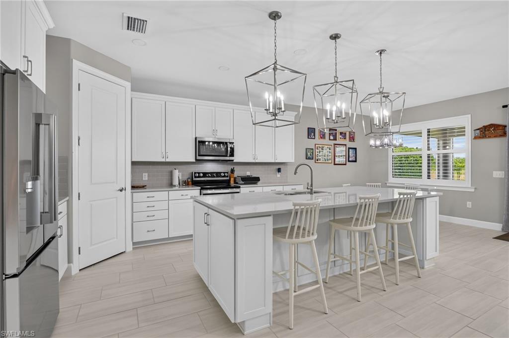 Spacious kitchen featuring white cabinetry, light countertops, stainless steel appliances, a center island with sink, and three geometric pendant lights