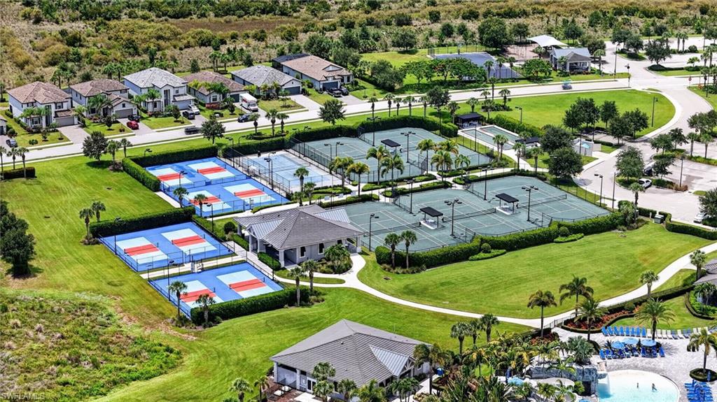 Recreational area featuring multiple sports courts, including blue and orange pickleball courts and green tennis courts, surrounded by manicured lawns and tropical landscaping