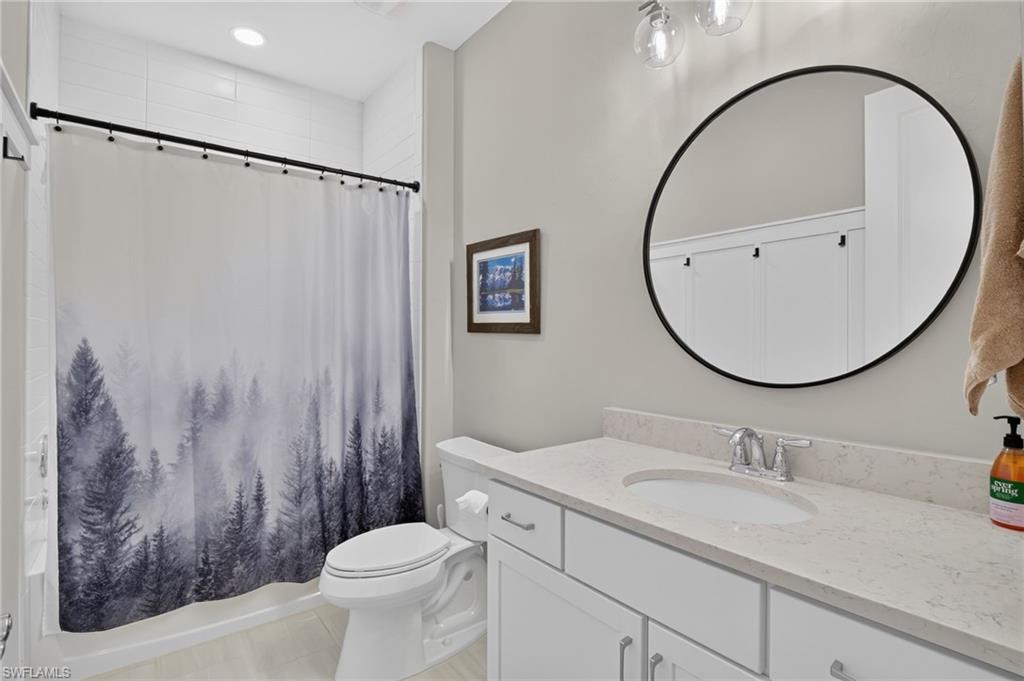 Bathroom featuring a white vanity with a light-toned countertop, an undermount sink, and a circular black-framed mirror