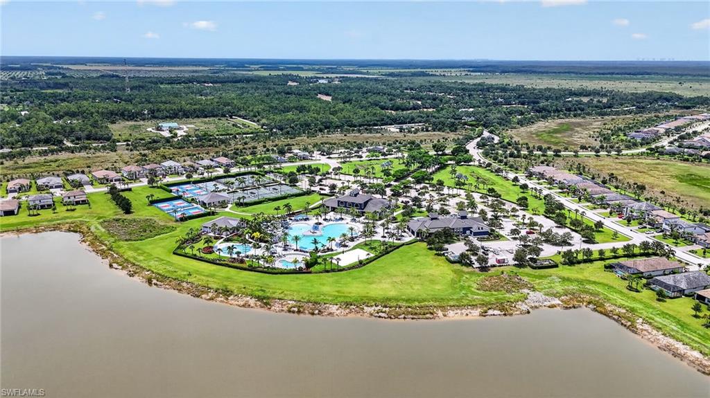 Aerial representation of a residential community featuring a prominent lakefront, extensive green spaces, a central recreation area with multiple swimming pools, sports courts, and a clubhouse structure