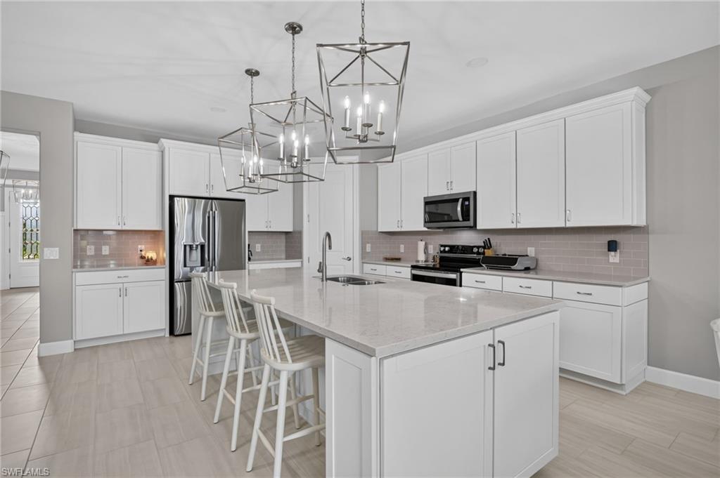 Modern kitchen featuring a large center island with integrated sink, white cabinetry with dark hardware, and a subway tile backsplash