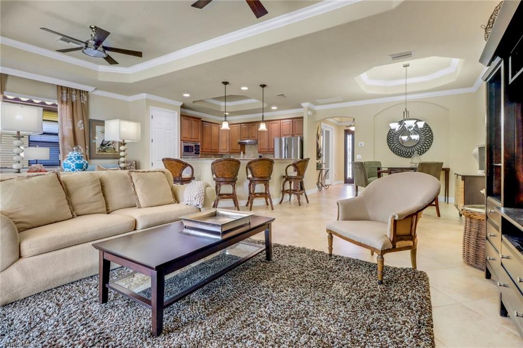Living area with a tray ceiling, ceiling fan, arched walkways, ornamental molding, and light tile patterned floors
