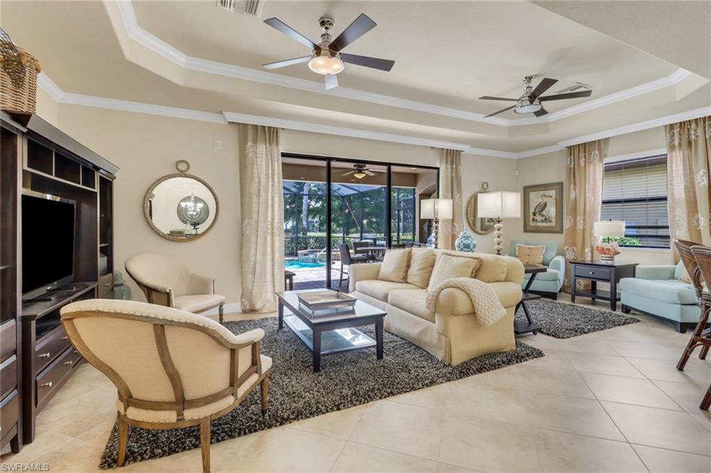 Living room featuring a tray ceiling, a ceiling fan, light tile patterned floors, and ornamental molding