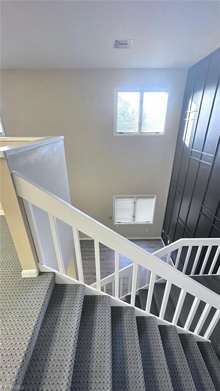 Two-story interior featuring a carpeted staircase with white railings, a textured accent wall, and multiple windows providing natural illumination