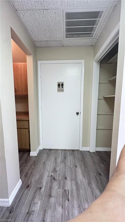 Hallway featuring wood-finish flooring, white trim, and a drop ceiling with an air vent