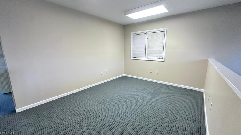 Carpeted room featuring a window with blinds, ceiling-mounted fluorescent lighting, and a partial wall element