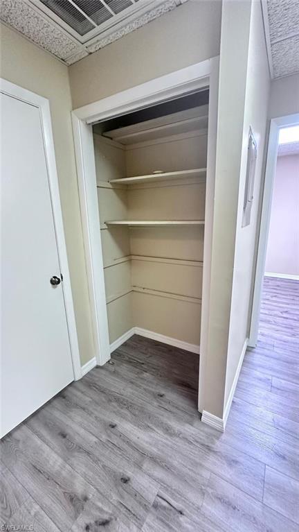 Storage closet with built-in shelving, wood-finish flooring, and painted baseboards