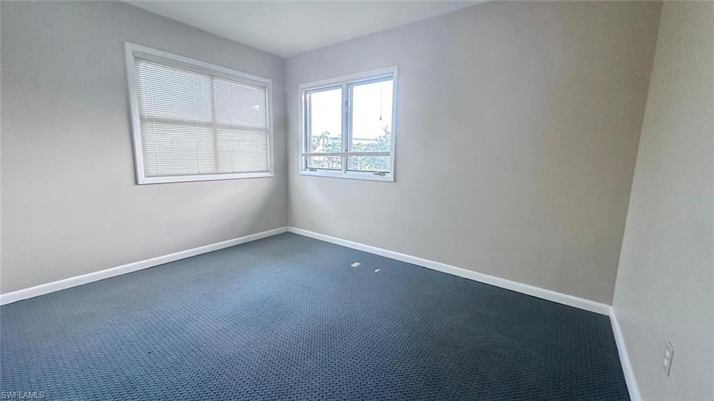 Room featuring two windows, neutral wall tones, and blue patterned carpeting
