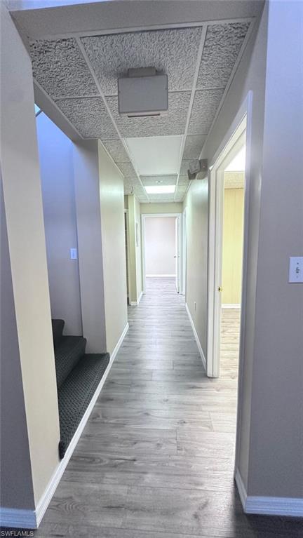 Hallway featuring wood-finish flooring, light tan wall paint, white trim, and a drop ceiling with recessed lighting