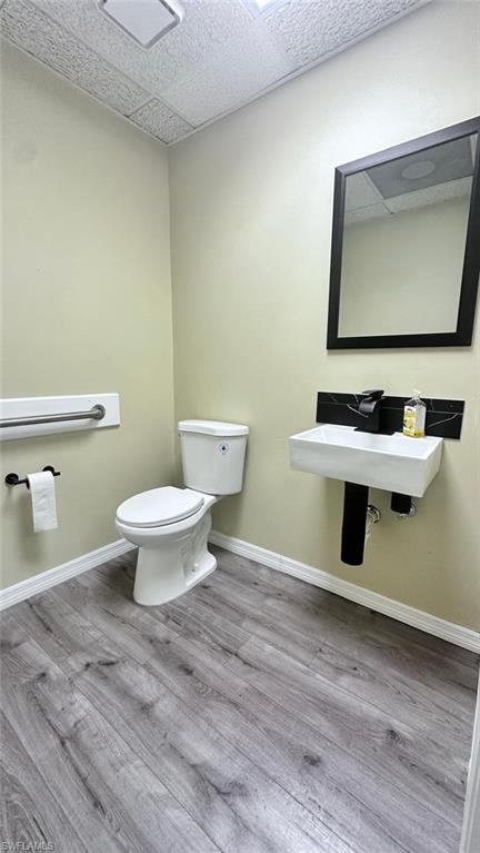 Powder room featuring wood-finish flooring, light-toned walls, and a modern wall-mounted sink with a black accent tile backsplash